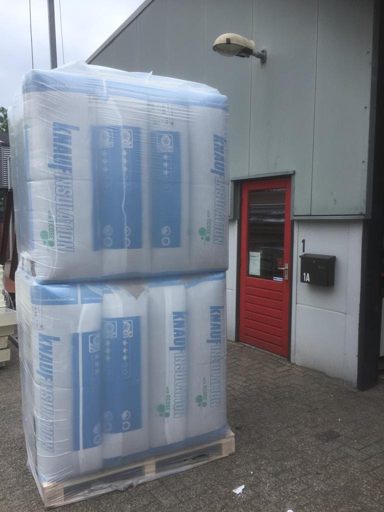 Twee pallets Knauf glaswol naast de rode deur van de hal