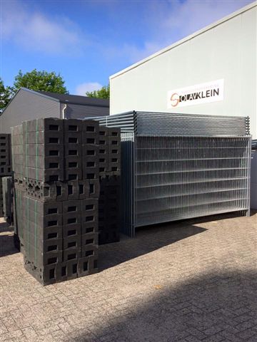 Bouwhekken en bouwhekvoeten op het terrein, met het bord van Olav Klein op de hal